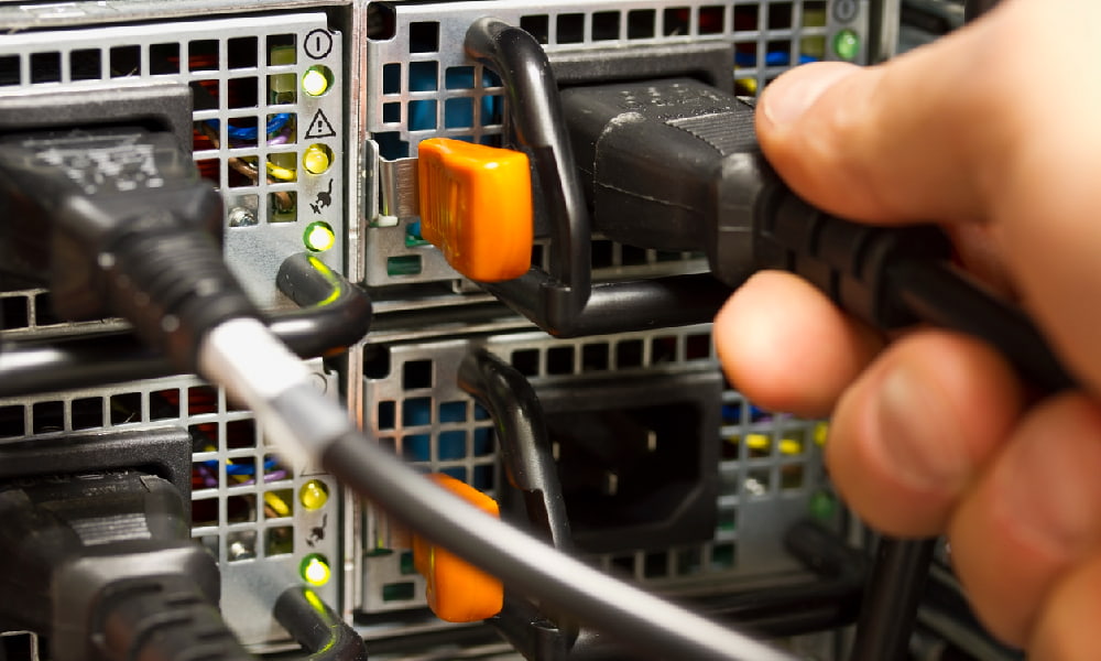 A person’s hand plugs a power cable into the PC power supply in the back of a computer.