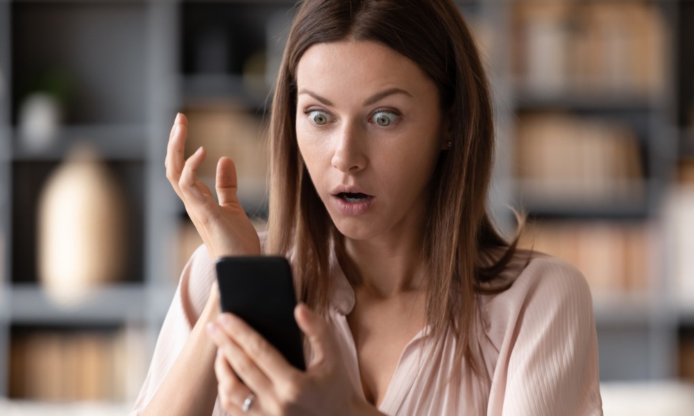 A woman using her smartphone is shocked by a smishing scam.